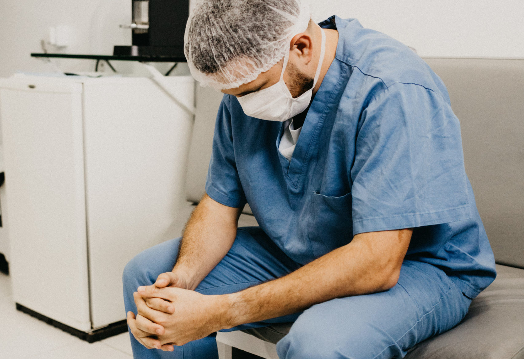 Man Wearing Blue Scrub Suit and Mask Sitting on Bench